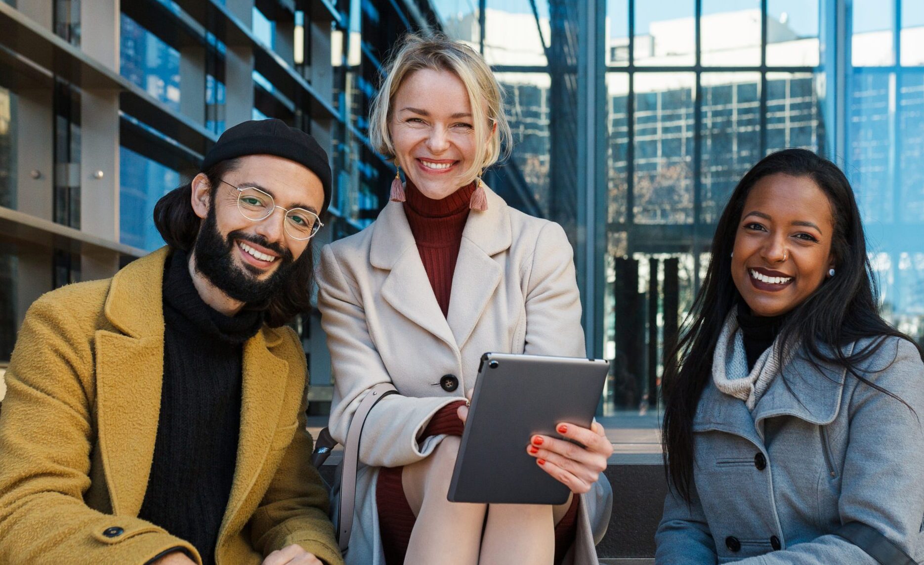 Business colleagues looking at camera and smile while sitting on the stairs outside the office building.